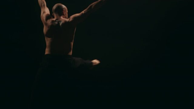 A ballet male dancer is performing jump pirouette and spinning on classic theater stage. Acrobatic elements of contemporary dance. Concept of professional choreography and performance. Slow motion.