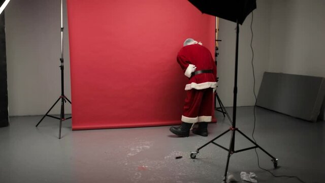 Stylish santa claus cleans up the photo studio after shooting or a holiday. Santa Claus collects candy from the floor with a vacuum cleaner.