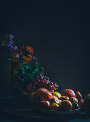 Dark baroque renaissance style still life photography of fruit and flowers. Apples, grapes, pomegranate, quince, mint and garden flowers.