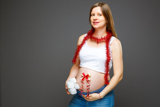Pregnant woman with big belly and baby booties, expecting baby birth on Christmas eve. Woman with stomach and new year decorations expecting a present for her baby.