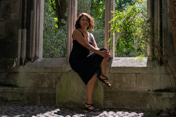 Elegant brunette woman with wavy hair and deep black eyes wearing a black dress, gazing out of a window with soft lighting