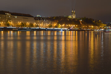 Fototapeta premium Night city with river, street lights are reflected in the water surface, in the background a historic building