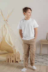 Minimalistic studio photo of eight old caucasian boy wearing in white t-shirt and beige pants for creating mockups for presentation graphic tees and pattern design