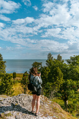 Woman with brown curly hair hiking and taking pictures with phone on the seaside by the Uugu cliff on the Muhu Island near Saaremaa in Estonia during a sunny day
