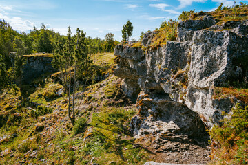 Uugu bluff or cliff on the Muhu Island in Estonia, located by the Baltic sea and near the island of Saaremaa. Beautiful sunny day with blue sky, white clouds, forest and stone cliffs by the seaside.