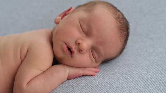 Newborn baby boy sleeping without clothes on blue fabric and holding hands under his head