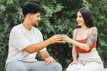 Two people toasting with soft drinks sitting in a park