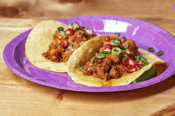 Traditional Mexican tacos with meat and vegetables in purple paper plates served for takeaway on wood table. Mexican food background.