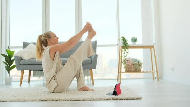 Woman making yoga and streight her legs online with tablet at home. Yoga exercices on distance with internet