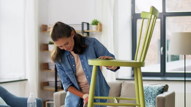 furniture renovation, diy and home improvement concept - happy smiling woman sanding old wooden chair with sponge