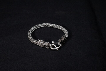 Fototapeta na wymiar Dragon heads silver bracelet on black cloth background