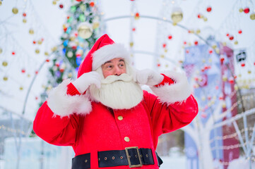 Portrait of an elderly man dressed as santa claus on the background of a christmas tree outdoors.