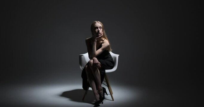 Beautiful fashion model sitting on chair with hand on chin over black background