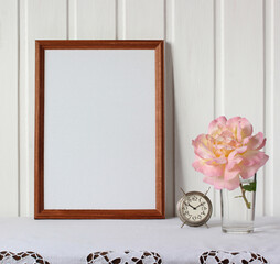 empty wooden frame on the table with retro alarm clock and rose