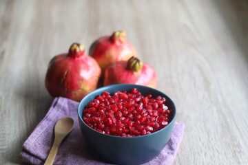 Bowl filled with pomegranate seeds and pomegranate fruit on a table. Selective focus.