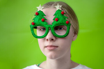 a girl in bright green glasses in the shape of a Christmas tree against a yellow background. Trends, party and crazy concept - Focus on glasses