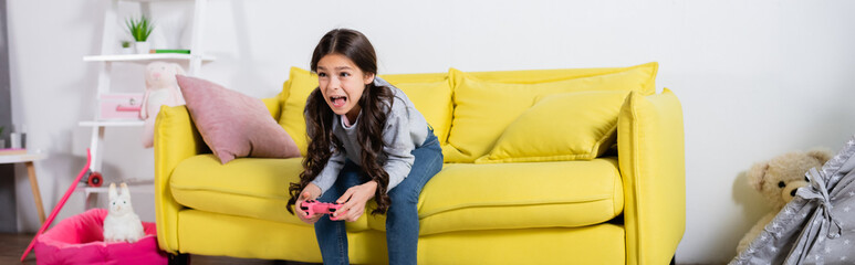 KYIV, UKRAINE - SEPTEMBER 17, 2021: preteen girl screaming while playing video game at home, banner. © LIGHTFIELD STUDIOS