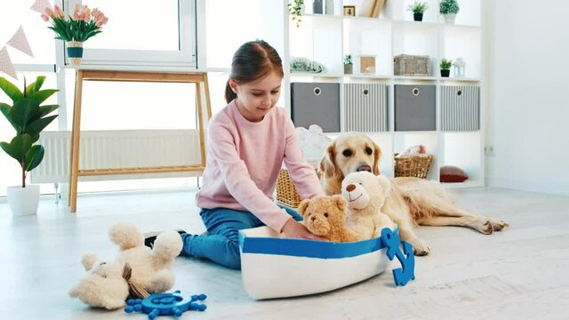 Little beautiful girl sitting on the floor with toys and marine ship and golden retriever dog lying next to her