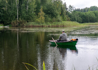 Fototapeta na wymiar a fisherman in a boat, calm lake water surface, tree reflections, cloudy day, fishing concept