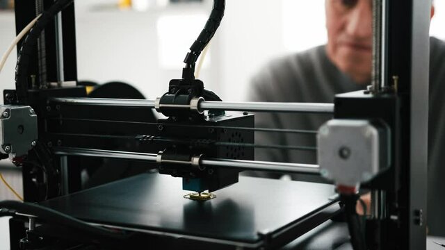 Closeup view of 3D printer work process and adult man engineer on blurred background