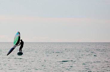 Man practicing wing foil with hydrofoil at sunset in the sea.