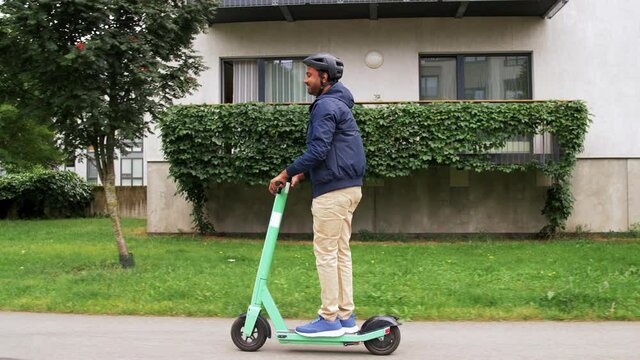 transport, safety and people and concept - happy smiling young man in helmet riding electric scooter on street