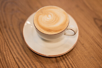 hot cappuccino coffee with milk foam in a white cup on a wooden table