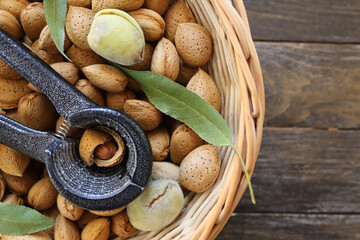 A basket willow full with an almonds in a shell with some green leaves and nutcracker on a dark...