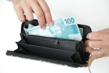 Nota de cédula de 100 reais na carteira preta e na mão na cor azul.
