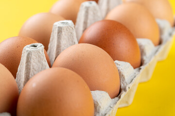 Chicken brown fresh raw eggs in an egg container n a yellow background. Ingredients for cooking....