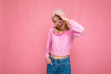 Photo of beautiful happy amusing young blonde female person isolated over pink background wall wearing trendy pink hat and pink blouse looking at camera and showing ok gesture