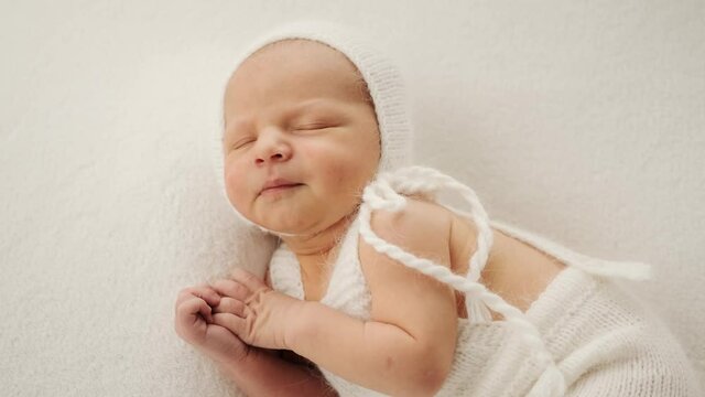Closeup portrait of adorable newborn baby sleeping wearing knitted white costume and hat. Cute infant child napping and smiling. Beautiful kid resting