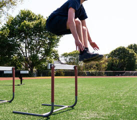 Athlete jumping over track hurdles on a green turf field
