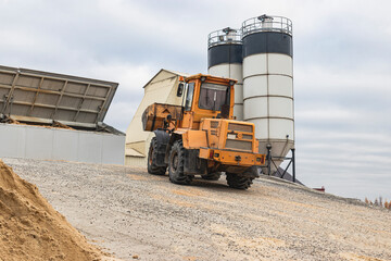 A powerful loader loads sand and crushed stone into a concrete plant. Industrial preparation of concrete. Heavy construction vehicle.