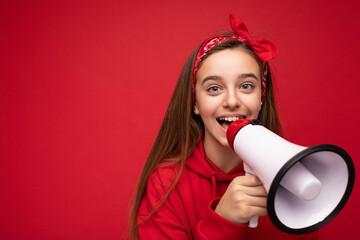 Portrait of beautiful attractive positive happy smiling dark blonde little female teenager with sincere emotions wearing stylish red hoodie and bandanna isolated over red background with copy space