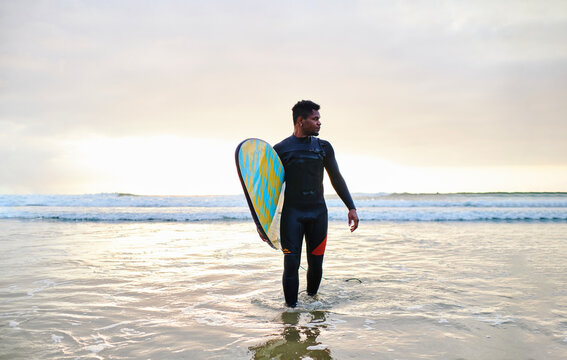 Surfer walking with surfboard on wet seashore in nature