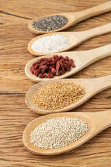 Assorted superfoods in spoons over wooden table. Chia, quinoa, oat, linseed and goji berry