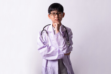 Thinking little boy Wearing medical doctor uniform playing holding glasses with stethoscope isolated on white.