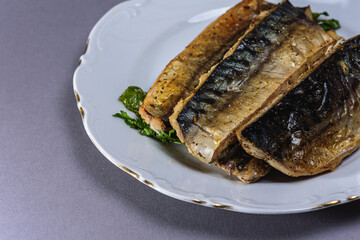 Fried mackerel with a short body file or Platoo in Thai is served on a white porcelain plate on a gray background. Popular fish menu in Thailand. (close-up, side view) 