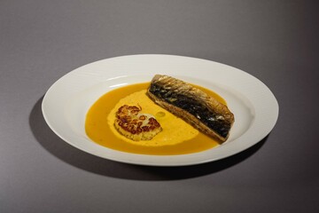 Baked mackerel fish with sauce and cauliflower and yellow puree in a white dish. Fish baked with vegetables. Gray background. Top view.
