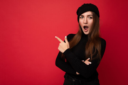 Portrait of beautiful fascinating emotional shocked female promoter pointing to the side at copy space for advertising wearing hipster outfit isolated over background wall with empty space with