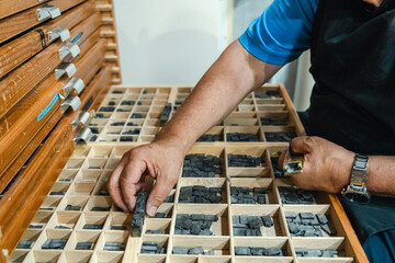 Crop serious elderly male master sitting at type case with lead letters for letterpress