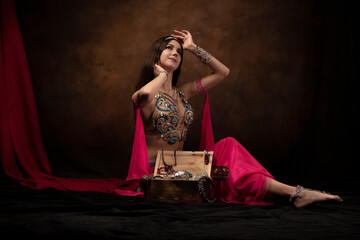 A girl in the image of an oriental princess is sitting next to a treasure chest. Oriental fairy tale, belly dance, Scheherazade.