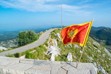 Waving flag of Montenegro against the background of mountains, near Njegos mausoleum in Lovcen National Park. Montenegro. Summer blue mountain landscape.