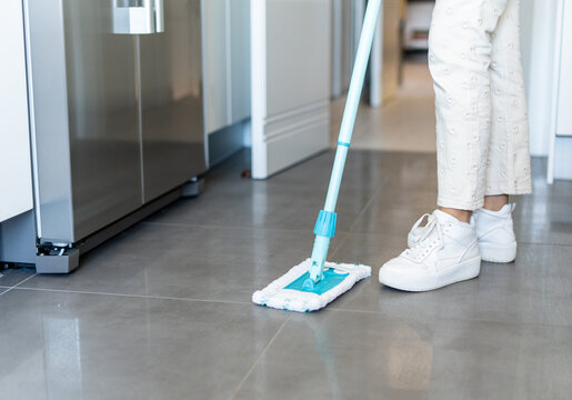Faceless woman cleaning floor with mop in kitchen