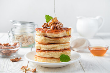 Pancakes with nuts and mint are pour with honey on a white background.