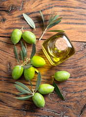 Green natural olives with bottle of olive oil on a vintage old wooden table.