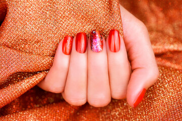 Brilliant festive red manicure. Female hand with a beautiful red manicure on a shiny red background.