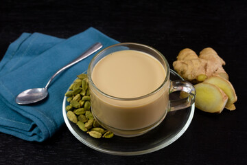 Glass cup of Masala chai tea with ginger and cardamom on black wooden background. Masala chai...
