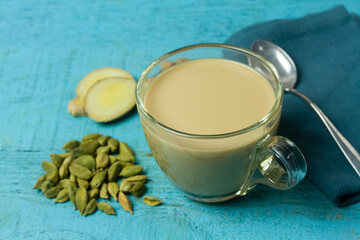 Glass cup of Masala chai tea with ginger and cardamom on blue wooden background. Masala chai popular traditional India hot drink made of milk, tea and spices.